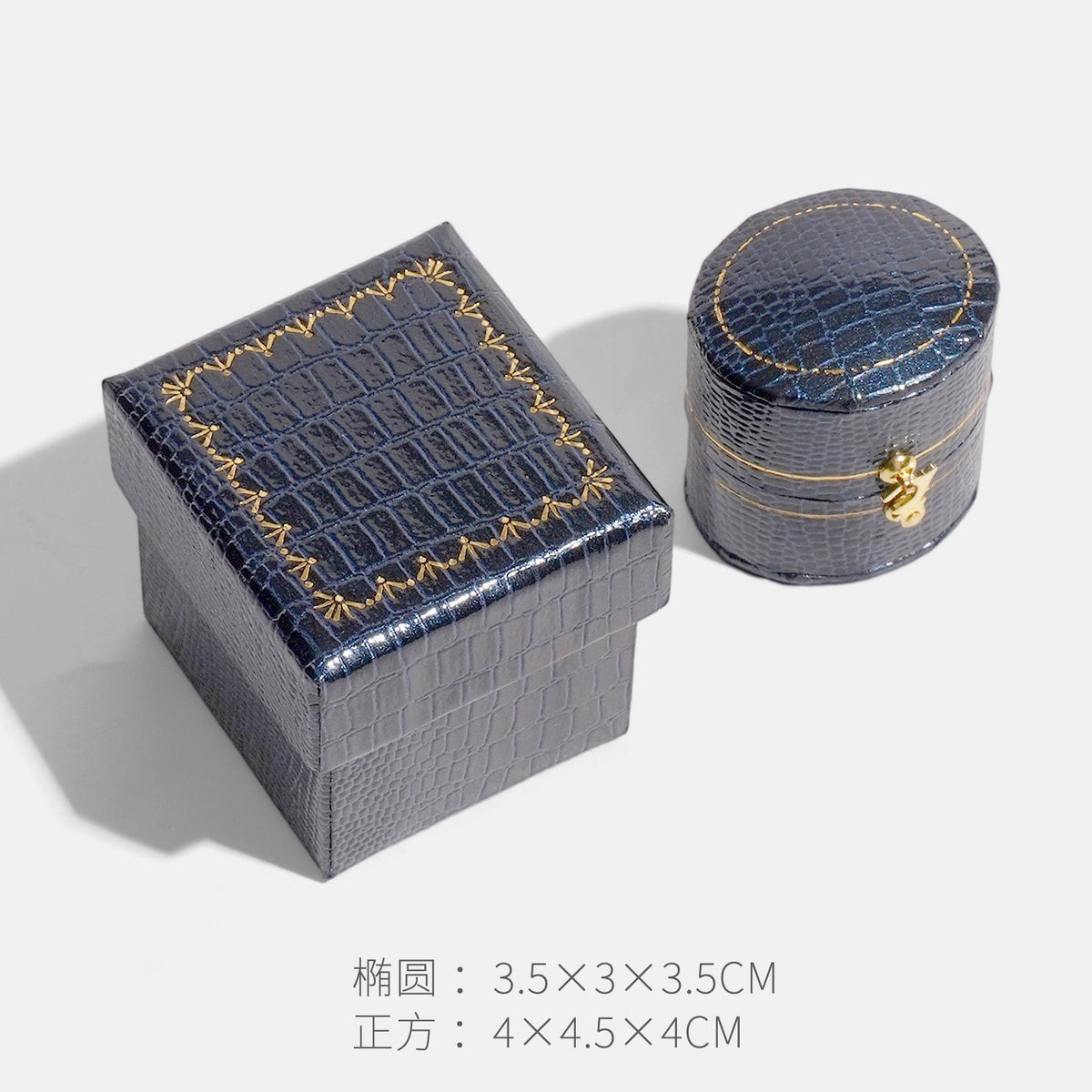 Dark blue crocodile textured oval clasp jewelry box beside a square box with gold border decoration