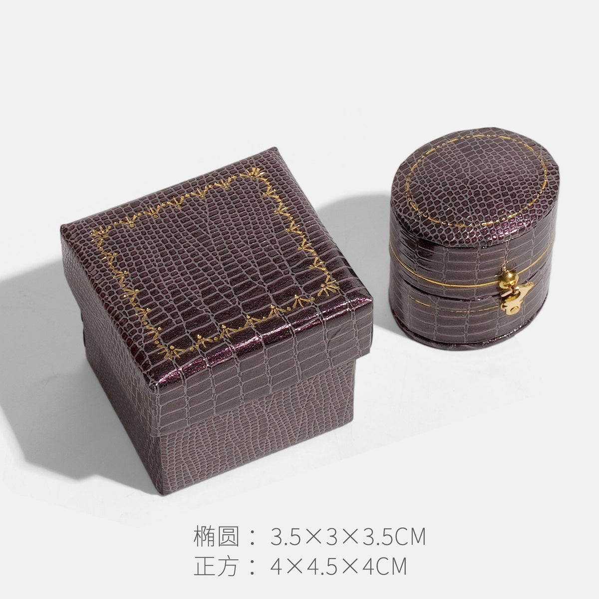 Dark burgundy crocodile textured oval clasp jewelry box beside a square box with gold border decoration