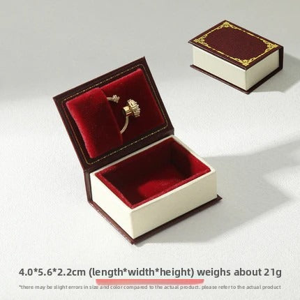 Burgundy book-shaped ring box with red ring cushion and matching closed box on white