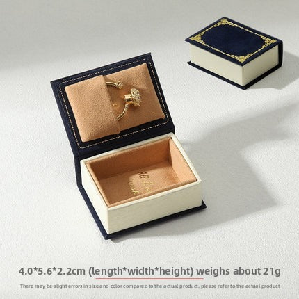 Navy book-shaped ring box with tan ring cushion and matching closed box on white