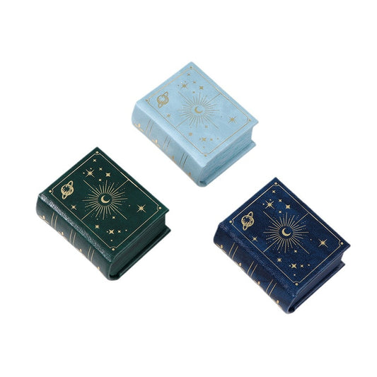 Closed celestial book-shaped ring boxes in light blue, green and navy