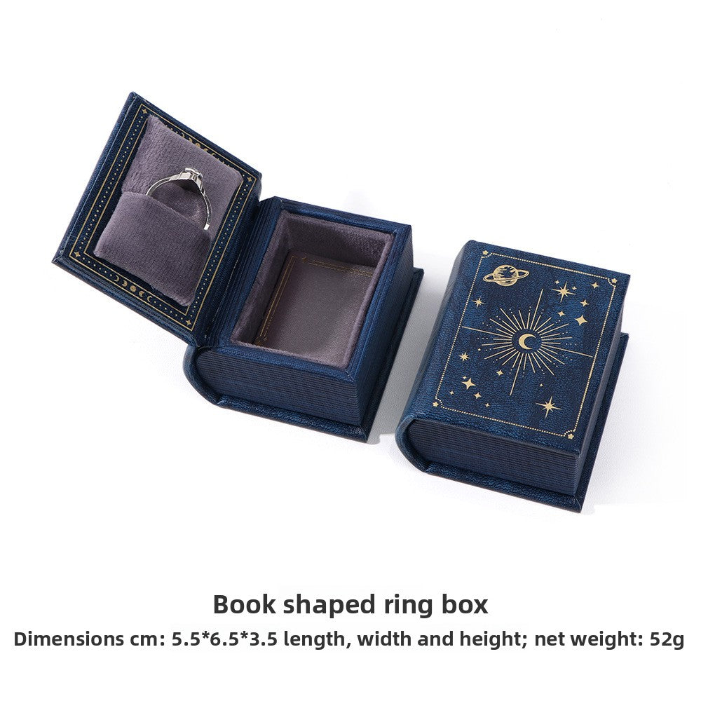 Navy book-shaped ring box with gold celestial decoration, shown open and closed