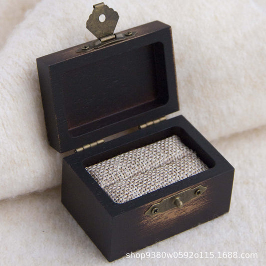 Dark scorched wooden ring box open with a single burlap ring slot